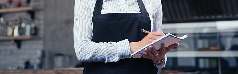 Best Front of House practices A chef with an apron is holding a writing pad and a pencil, writing down notes.